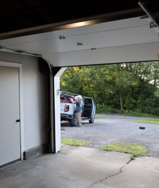 View from inside a garage showing a technician near a branded service truck while installing or repairing a garage door.