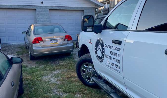 Bear Door Services van parked outside a residence with two garage doors, highlighting the company's readiness and mobility for on-site repairs and installations.